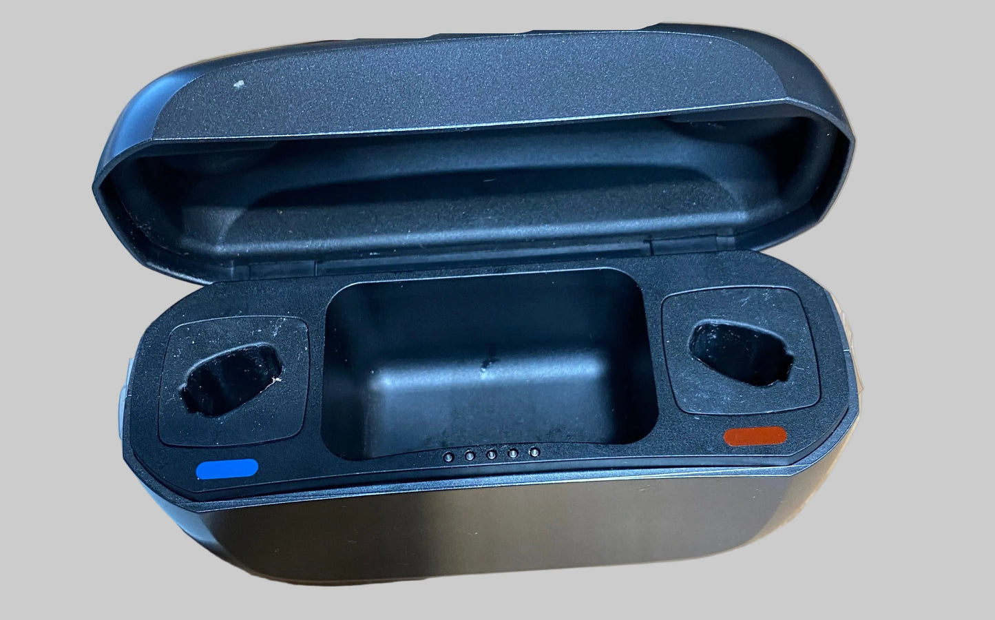 A black plastic charging dock or battery compartment shown open on a desk