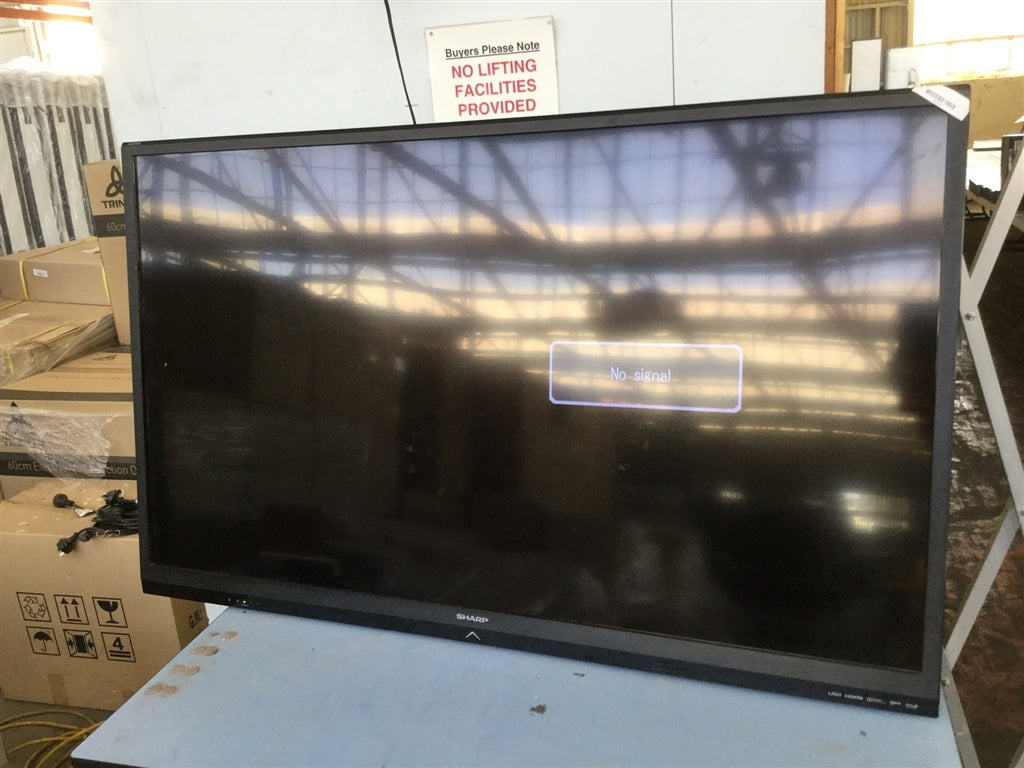 Large flat-screen monitor on a table with boxes and a 'No Lifting' sign in the background
