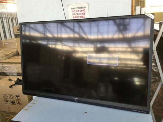 Large flat-screen monitor on a table with boxes and a 'No Lifting' sign in the background