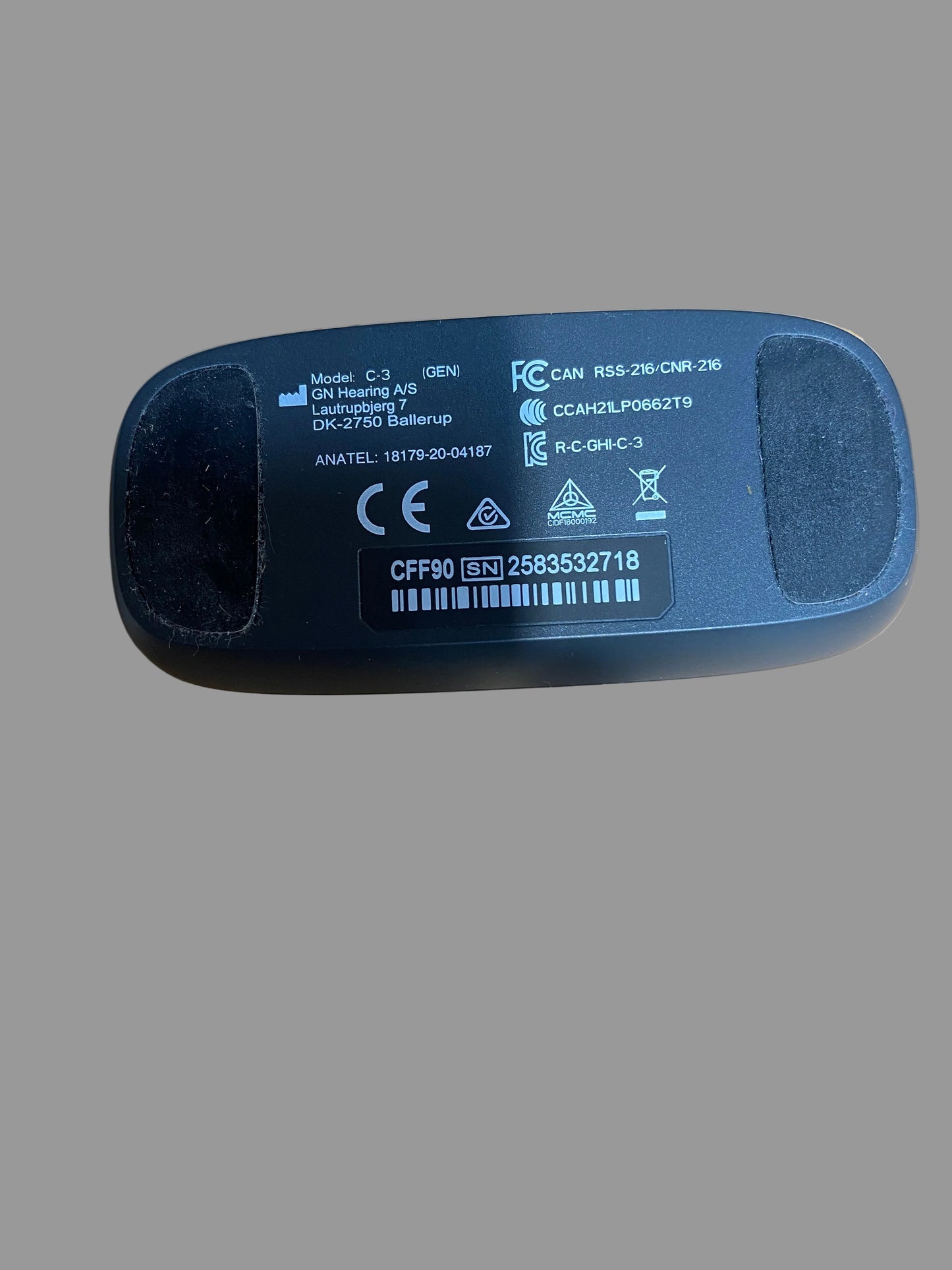 A close-up shot of the bottom of a black plastic electronic device, showing printed specifications, barcodes, and regulatory marks, resting on a brown cardboard surface.